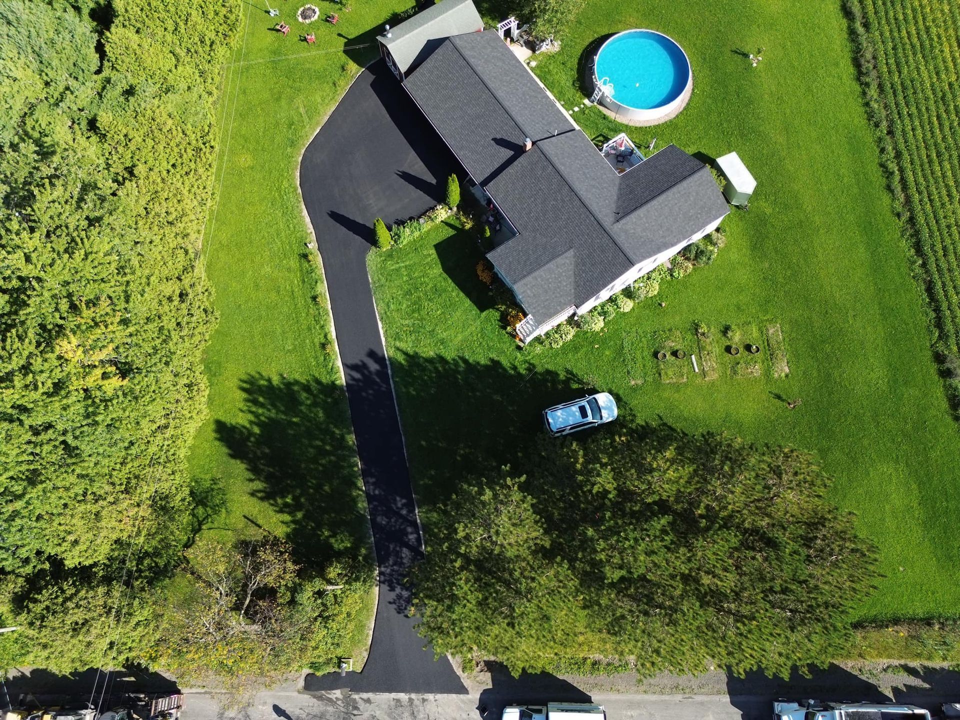 Aerial view of a house with a driveway, green lawn, and a round blue swimming pool.