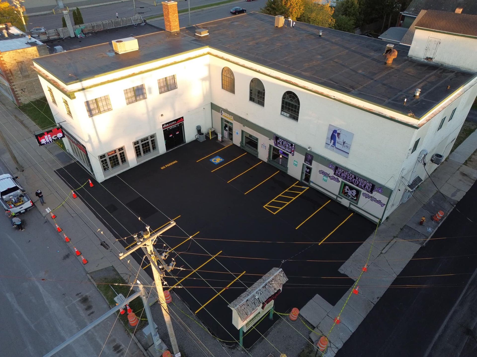 Aerial view of a commercial building with a mostly empty black parking lot and marked spaces at dusk