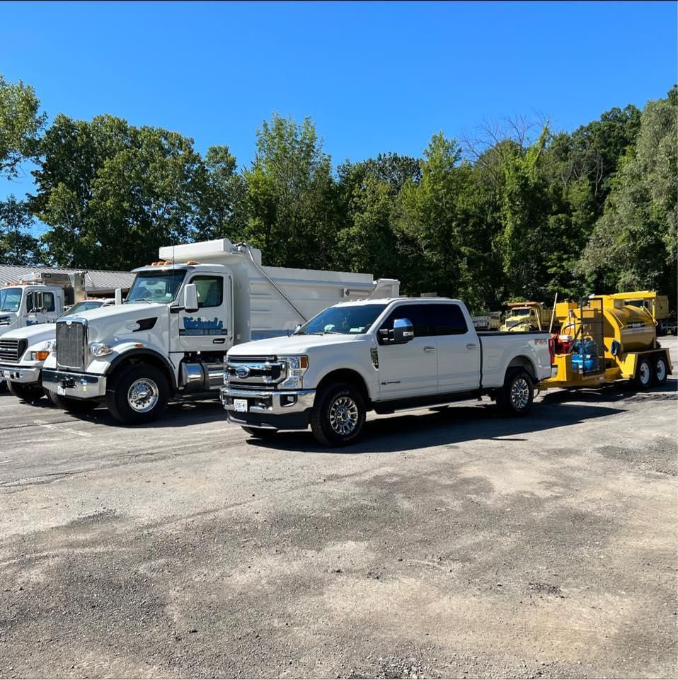 White work trucks and yellow equipment parked on a gravel lot under a clear blue sky.