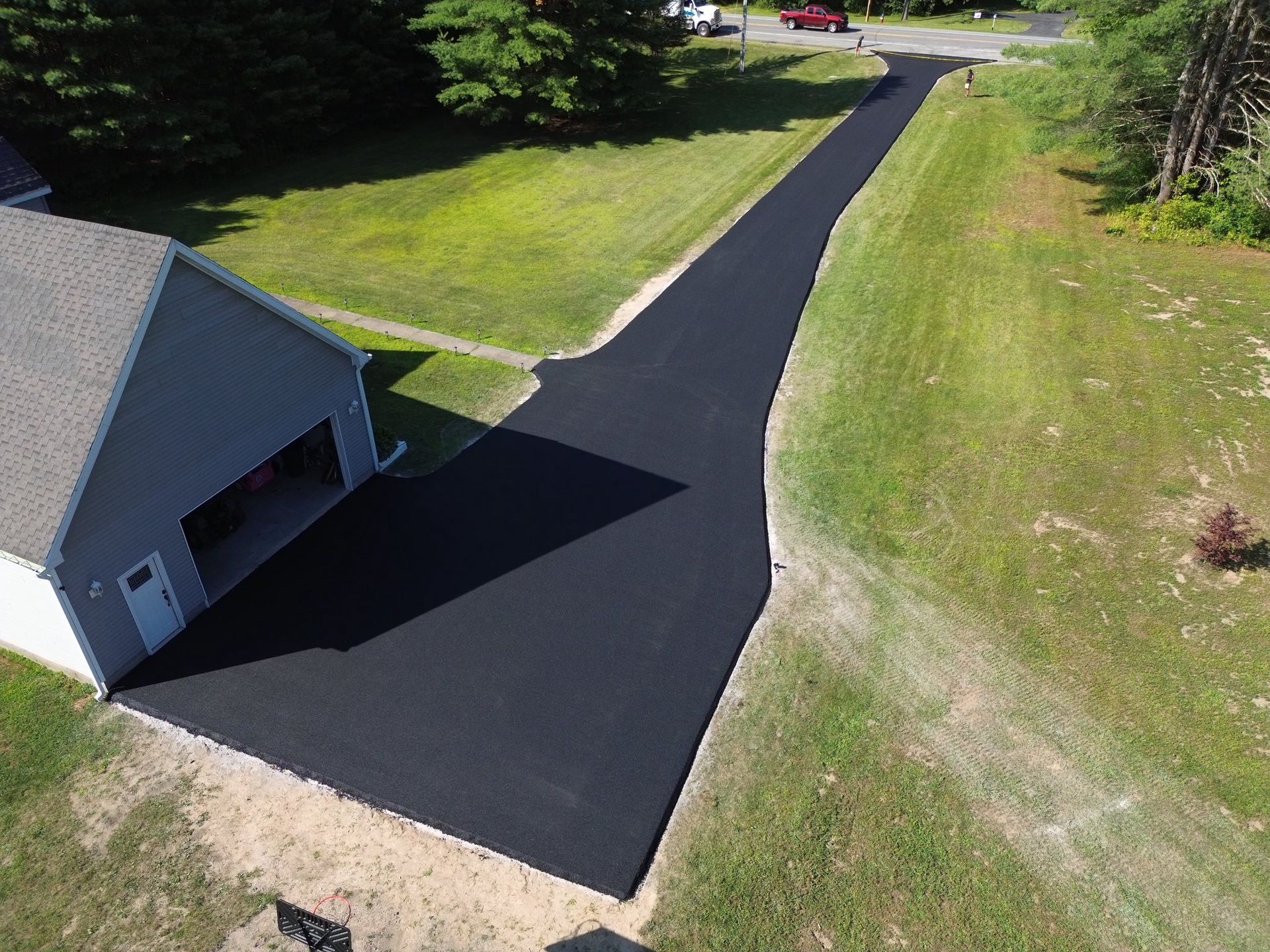 Fresh black asphalt driveway curving past a garage across a green lawn