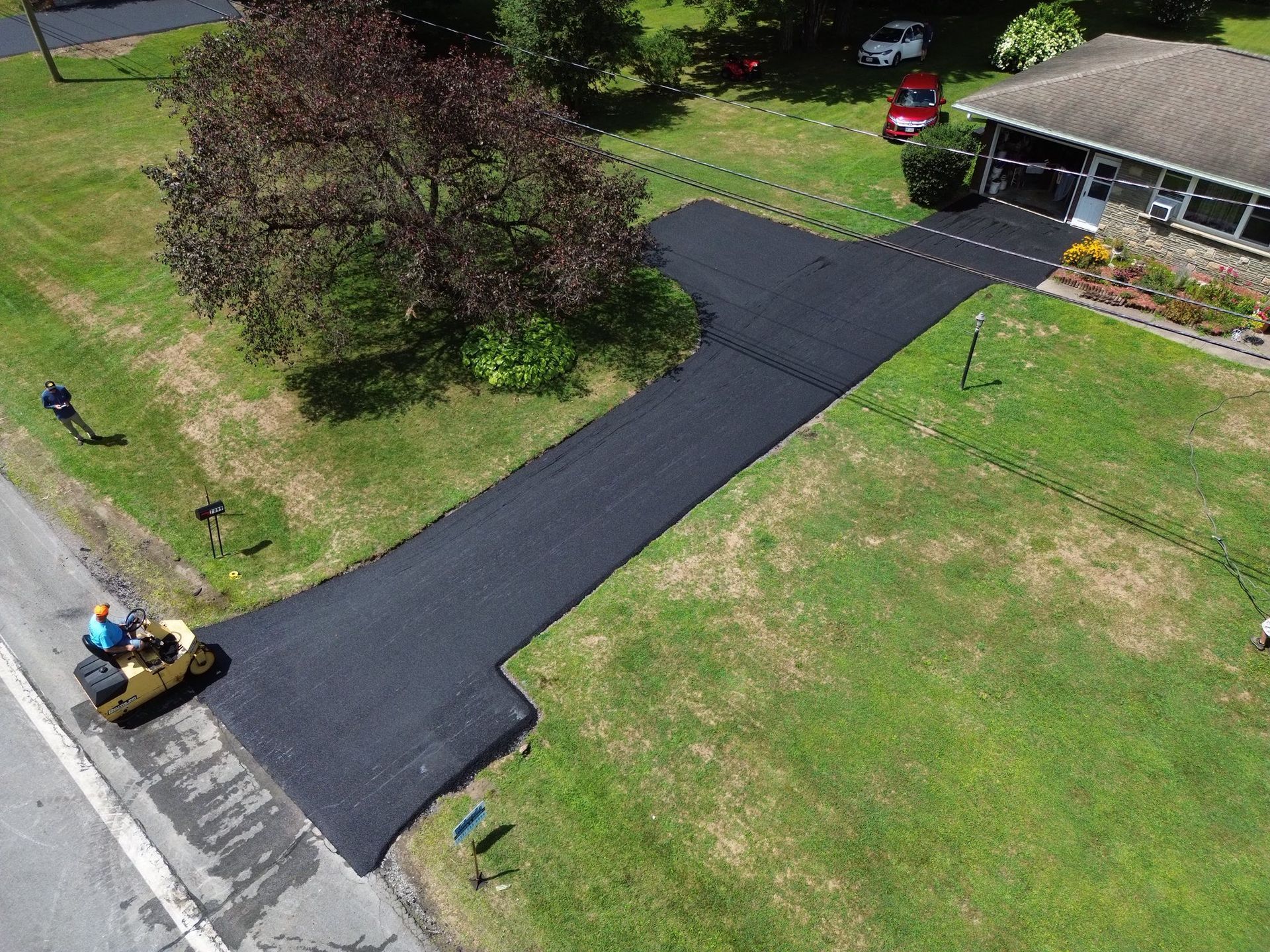 Freshly paved black driveway leading to a house, with workers and equipment nearby.