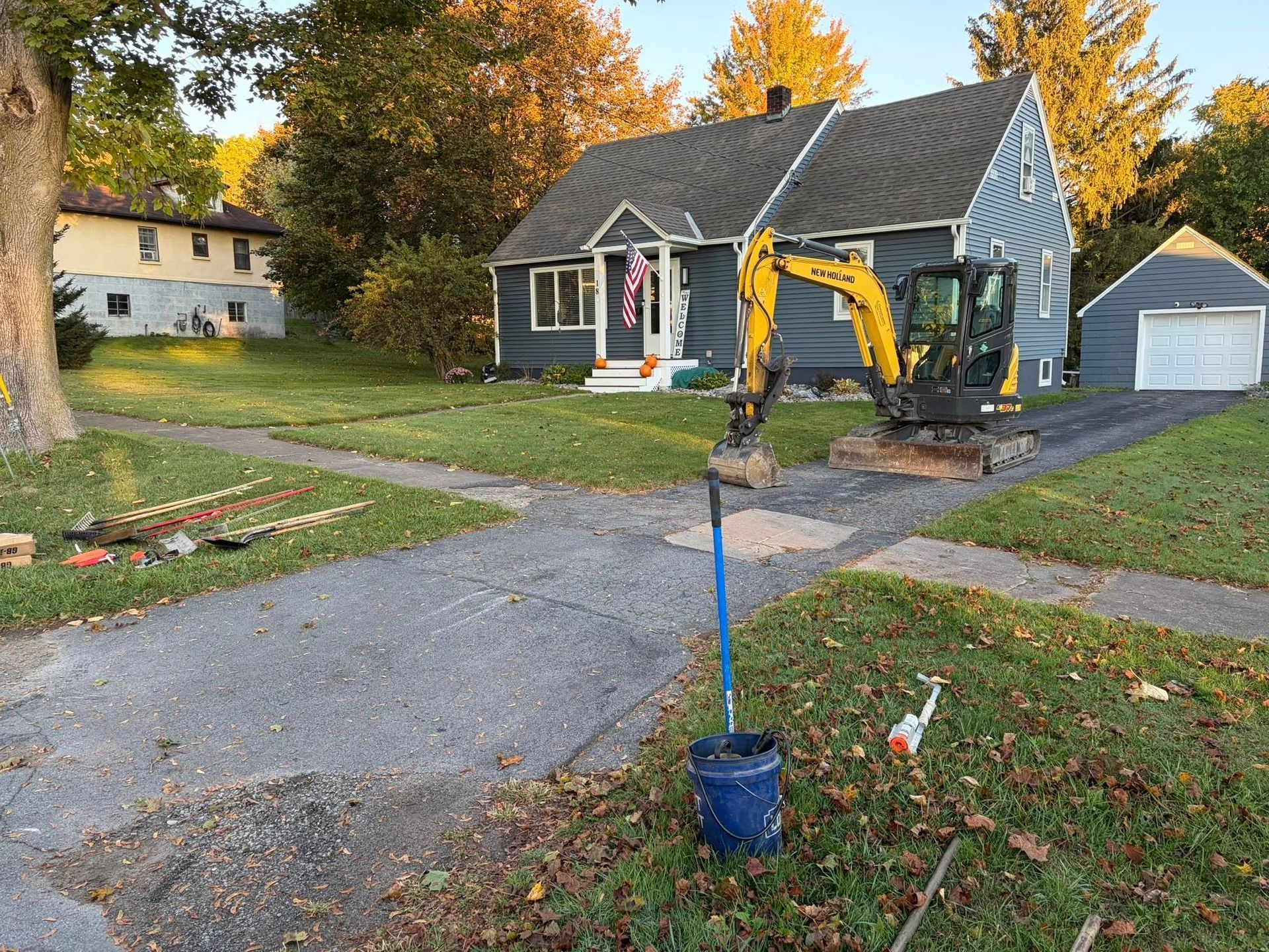 Small house with a yellow excavator digging a trench by the driveway in a suburban yard