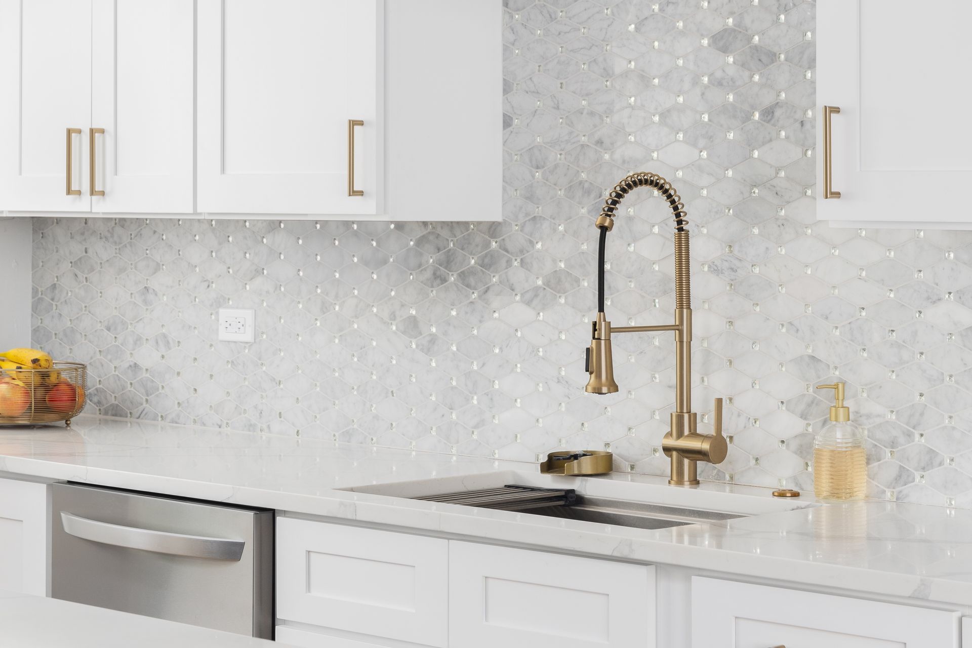 Bright white kitchen with gold faucet, speckled backsplash, and stainless steel sink and dishwasher