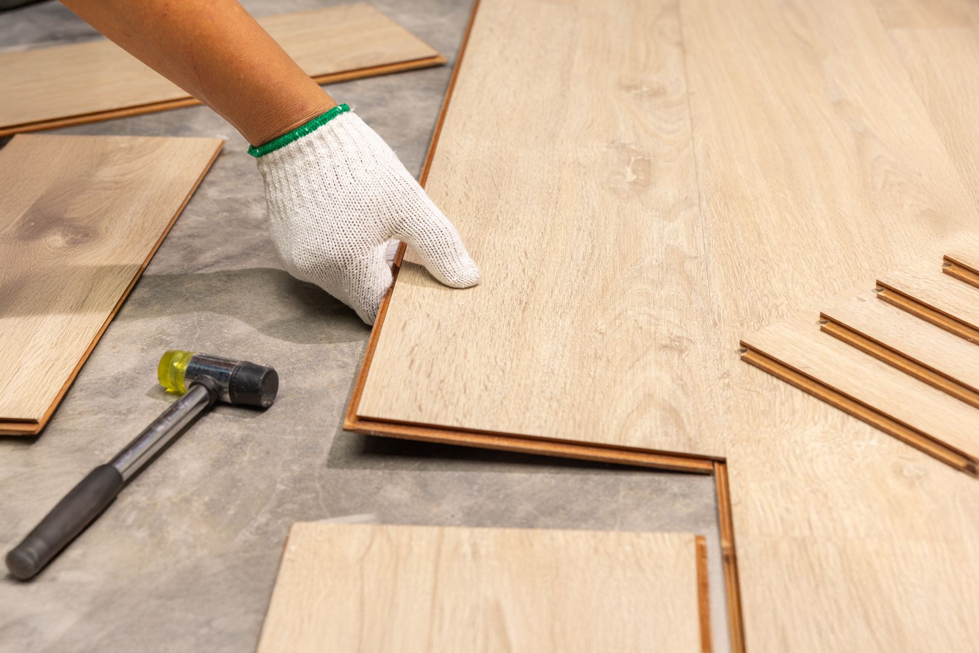 Gloved hand aligning wood laminate planks beside a hammer during floor installation