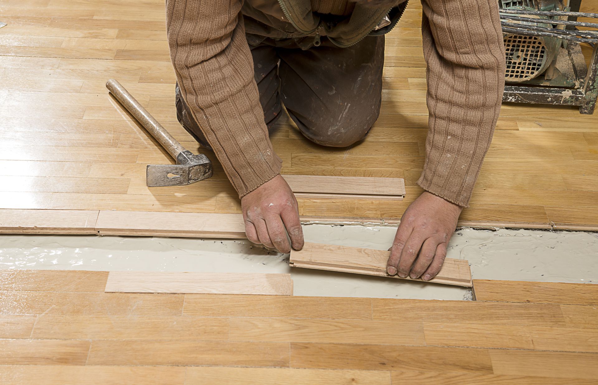 Person kneeling on a wooden floor measuring and cutting a strip of wood with a saw.