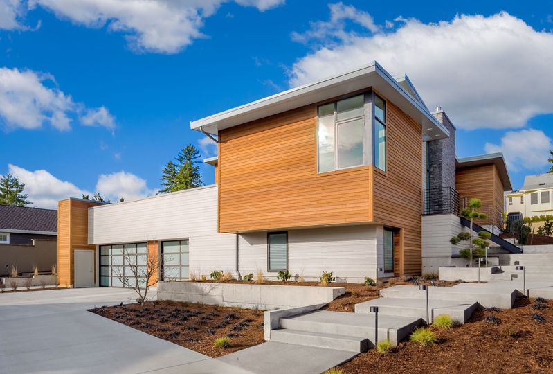 Modern two-story house with wood siding, white panels, and landscaped front steps under a blue sky