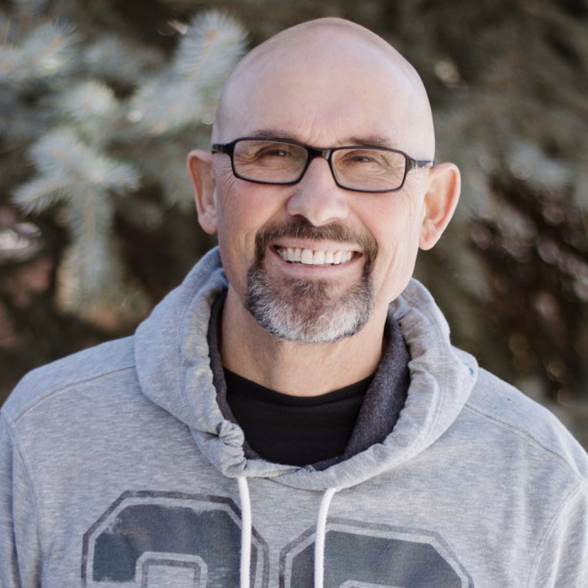 A bald man with glasses and a beard is smiling