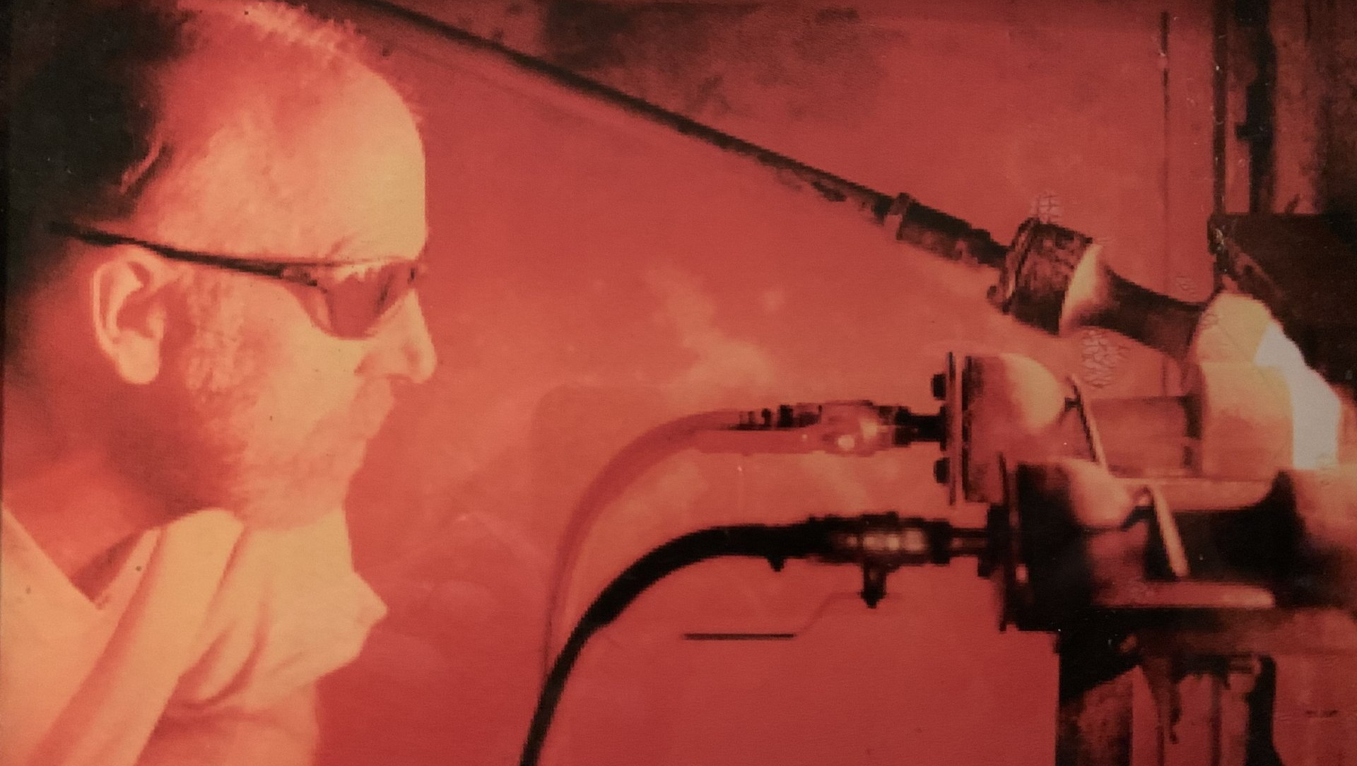 A man wearing sunglasses is looking at a machine with a red light behind him.