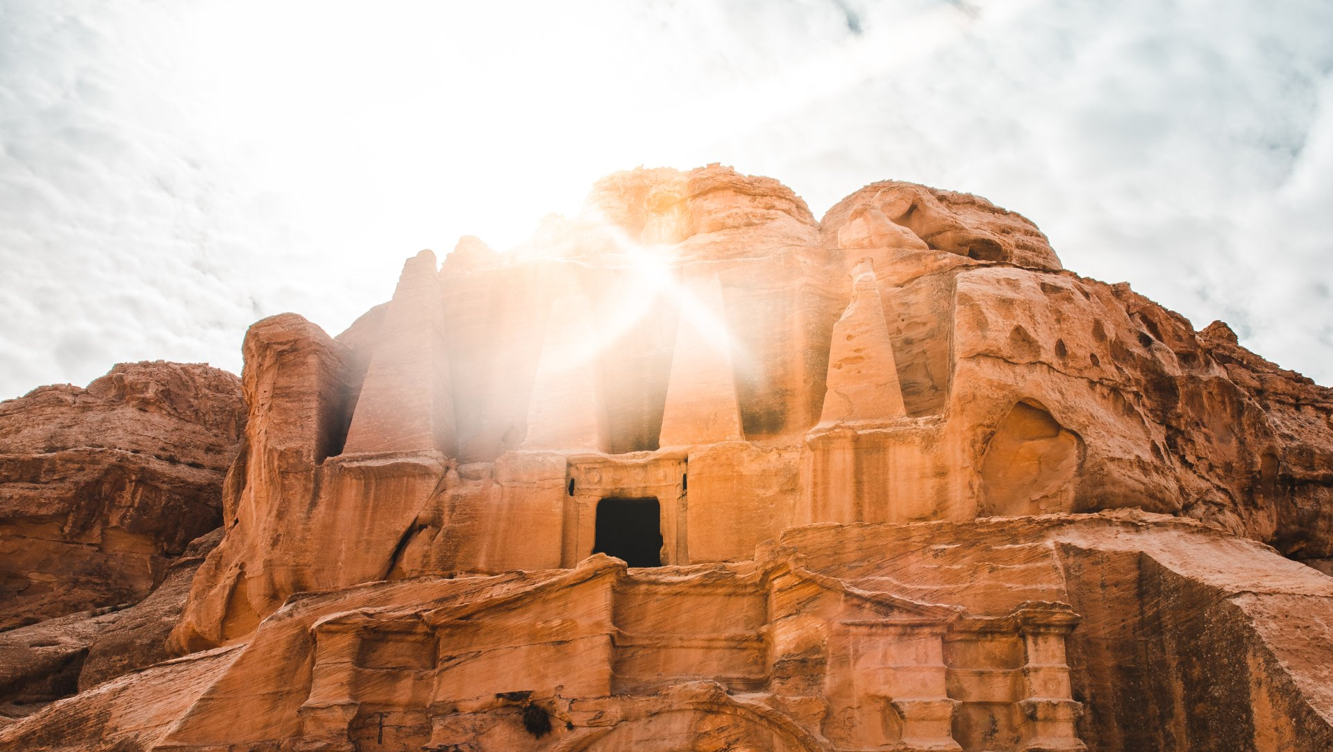 The sun is shining through the clouds on a rocky hillside.
