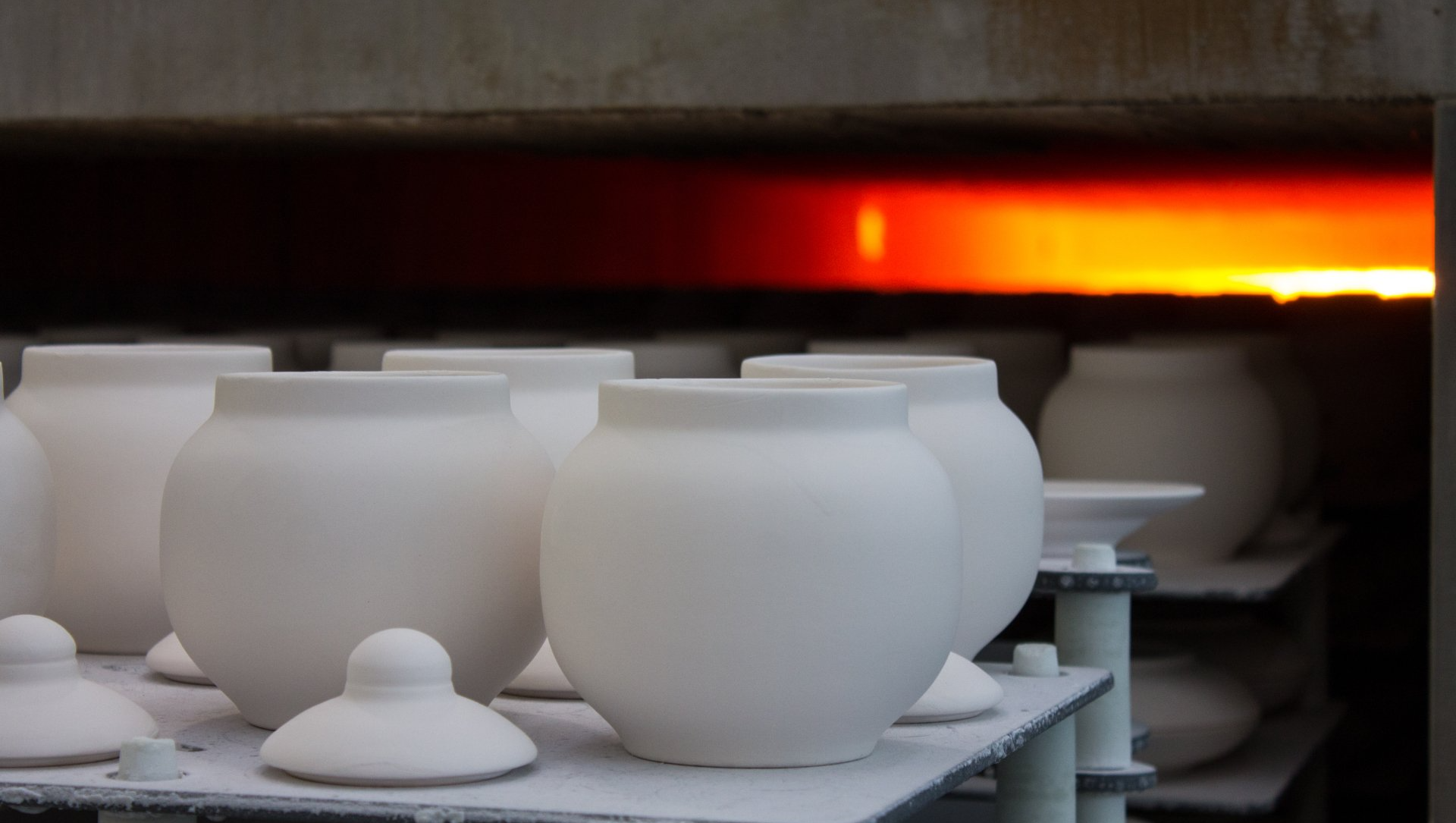 A bunch of white vases are sitting on a shelf in front of a fire