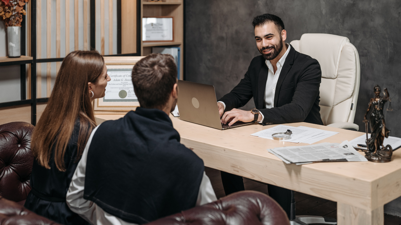 Couple consulting with a smiling professional at a desk, with laptop and papers, in an office setting.