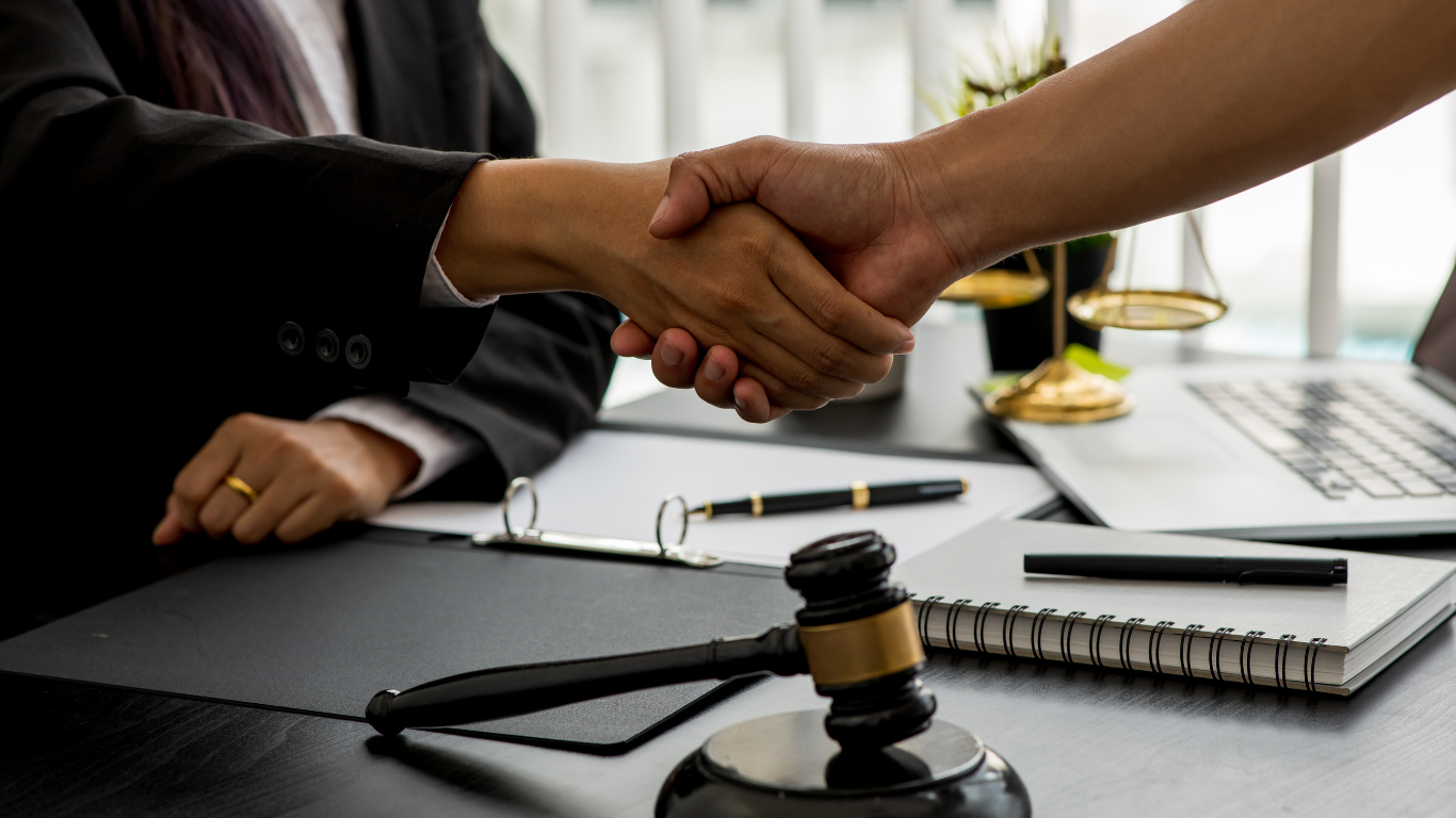 A man and a woman are shaking hands in front of a judge 's gavel.