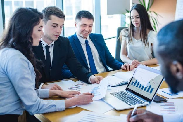 Business colleagues reviewing financial data at a conference table; graph on a laptop screen.