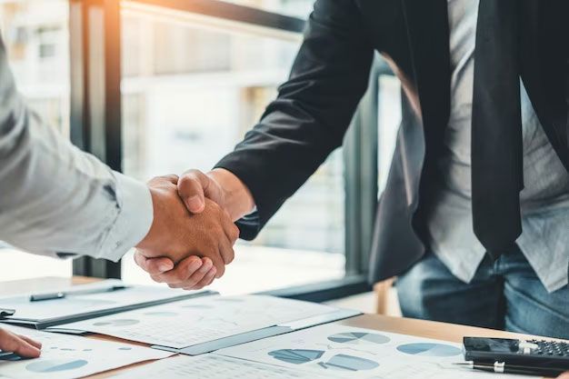 Two businesspeople shaking hands over a table with papers and a calculator.