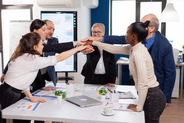 Team of people join hands over a table in an office, celebrating success.