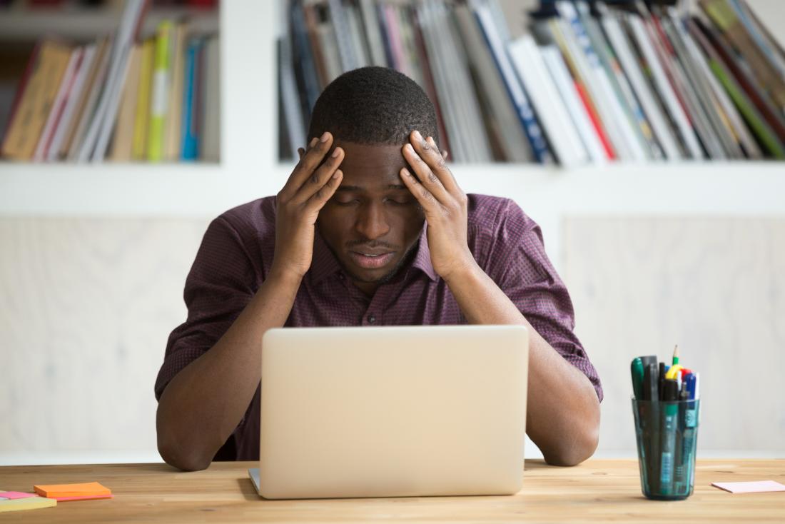 Man with hands on head looking at a laptop with a stressed expression.
