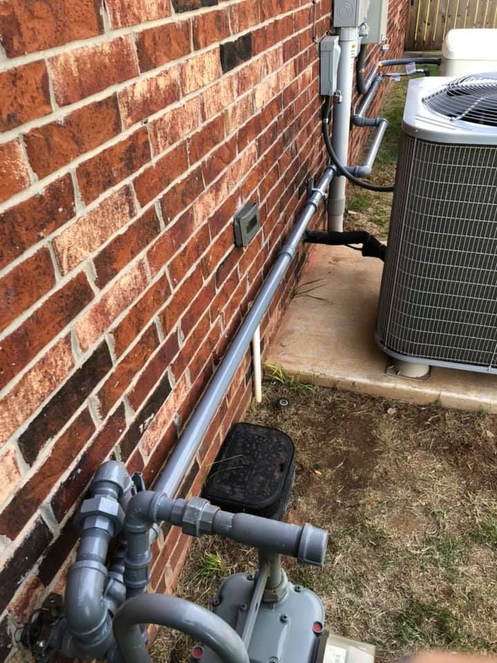 Gas and air conditioning unit with gray piping along a red brick wall.