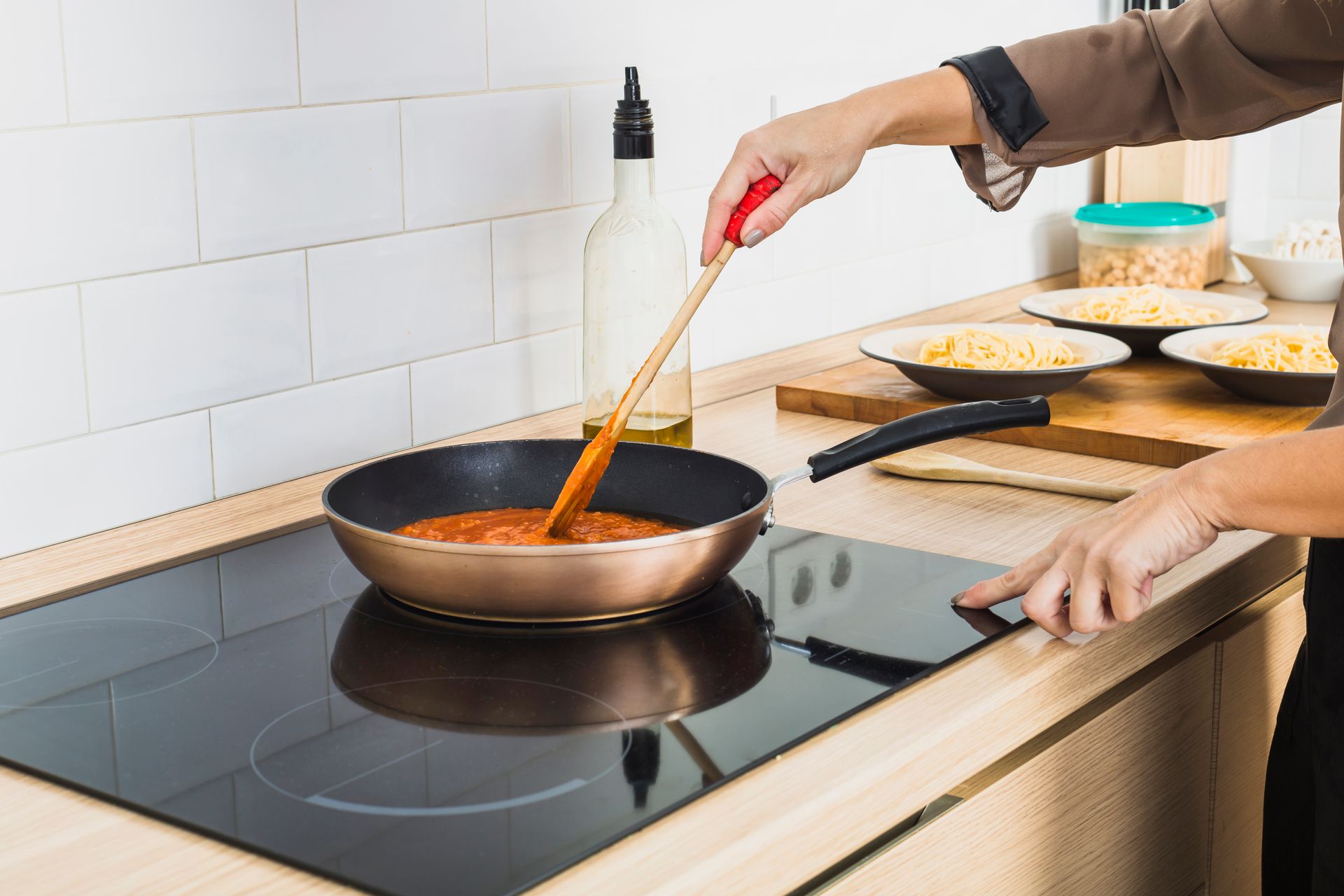 Person stirring sauce in a pan on a stovetop, kitchen setting.