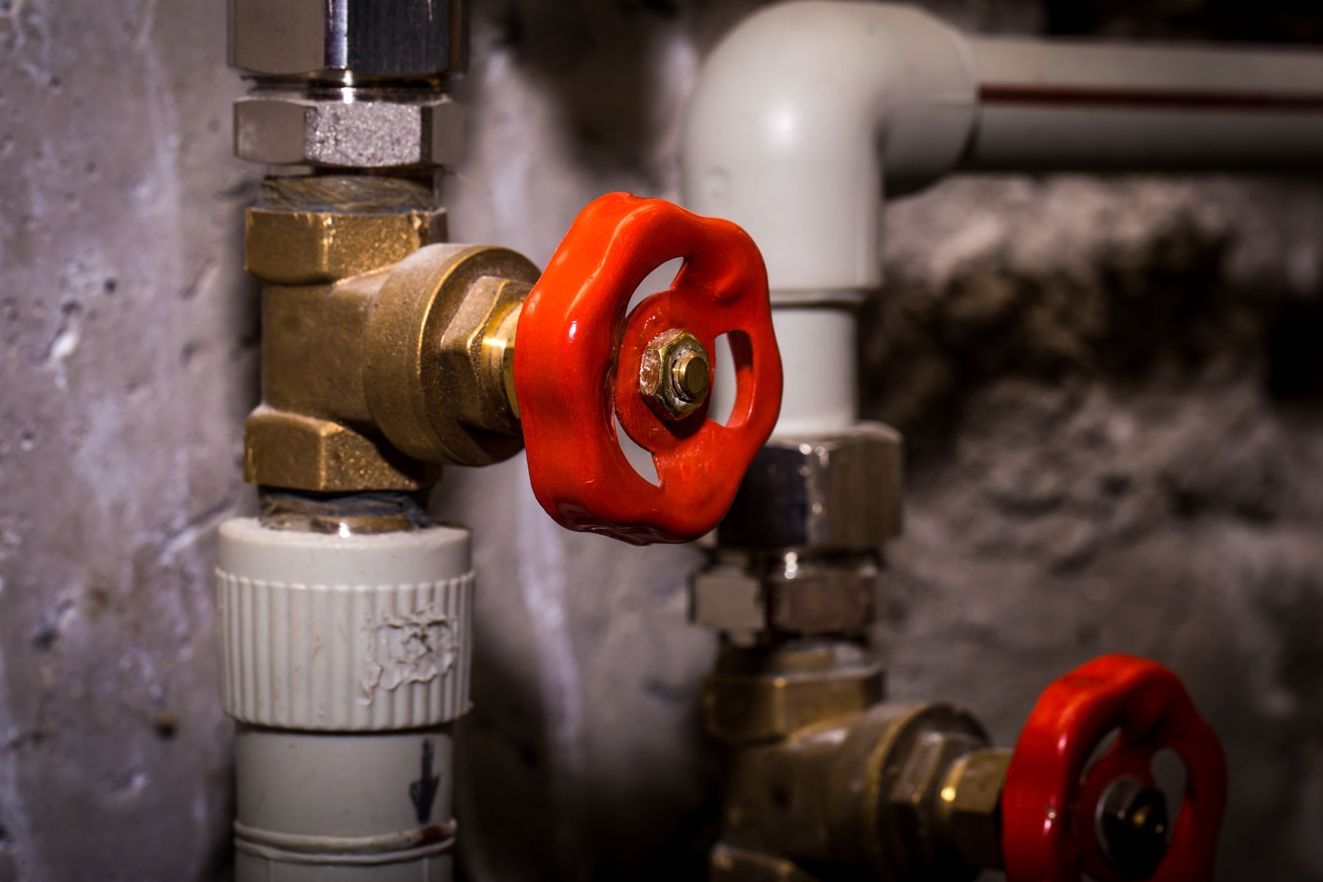 Close-up of brass and white pipes with red valves against a concrete wall.