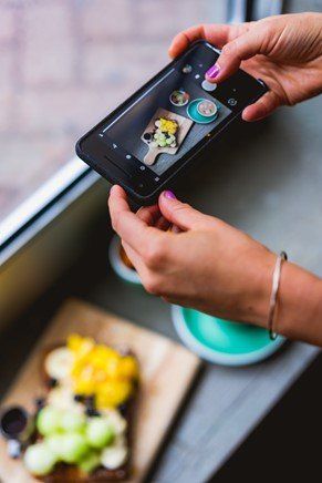 A woman clicking pictures of her food next to a window for natural lighting.