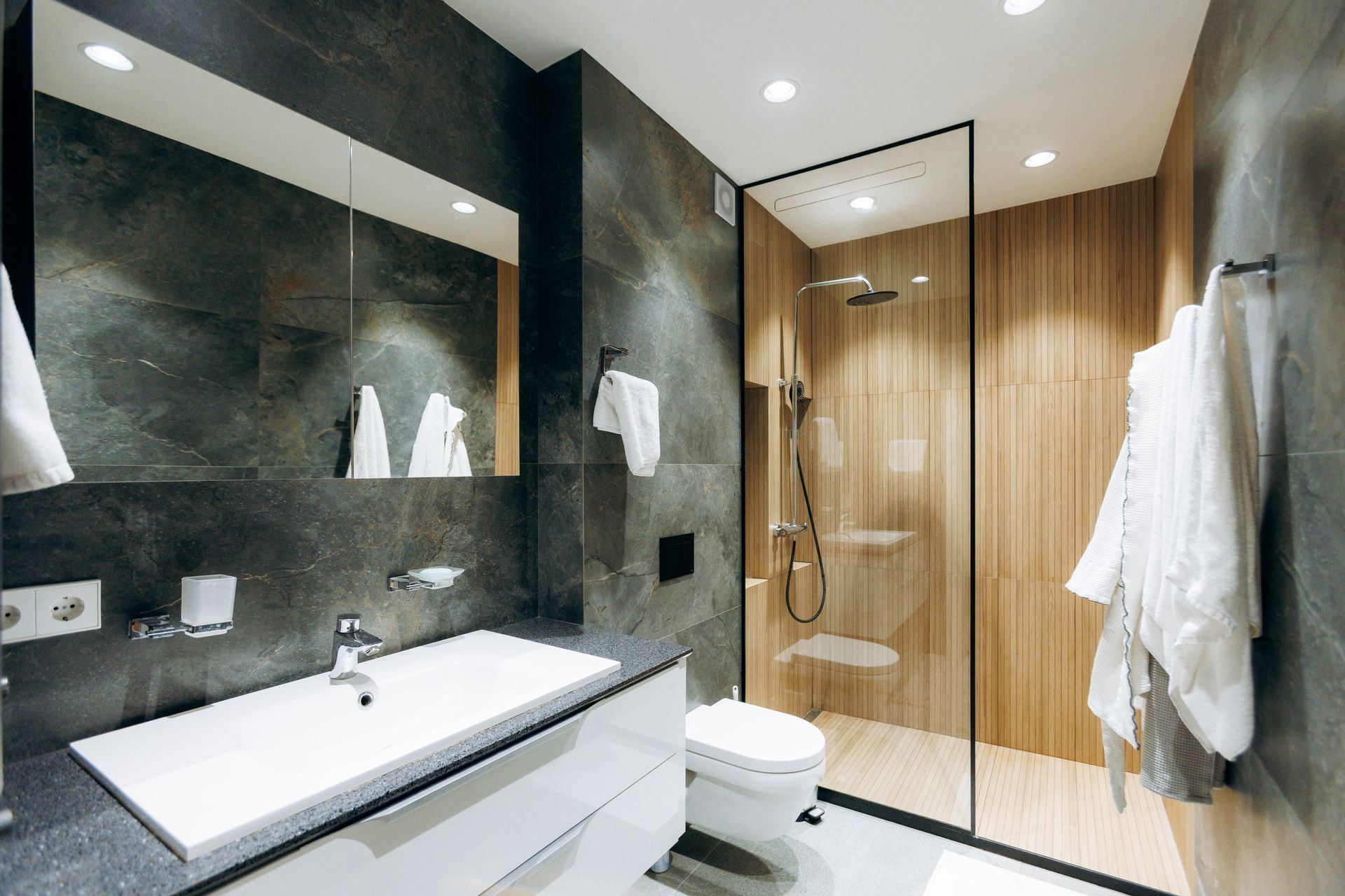 Modern bathroom with marble sink, large mirror, glass shower, and wood-paneled wall.