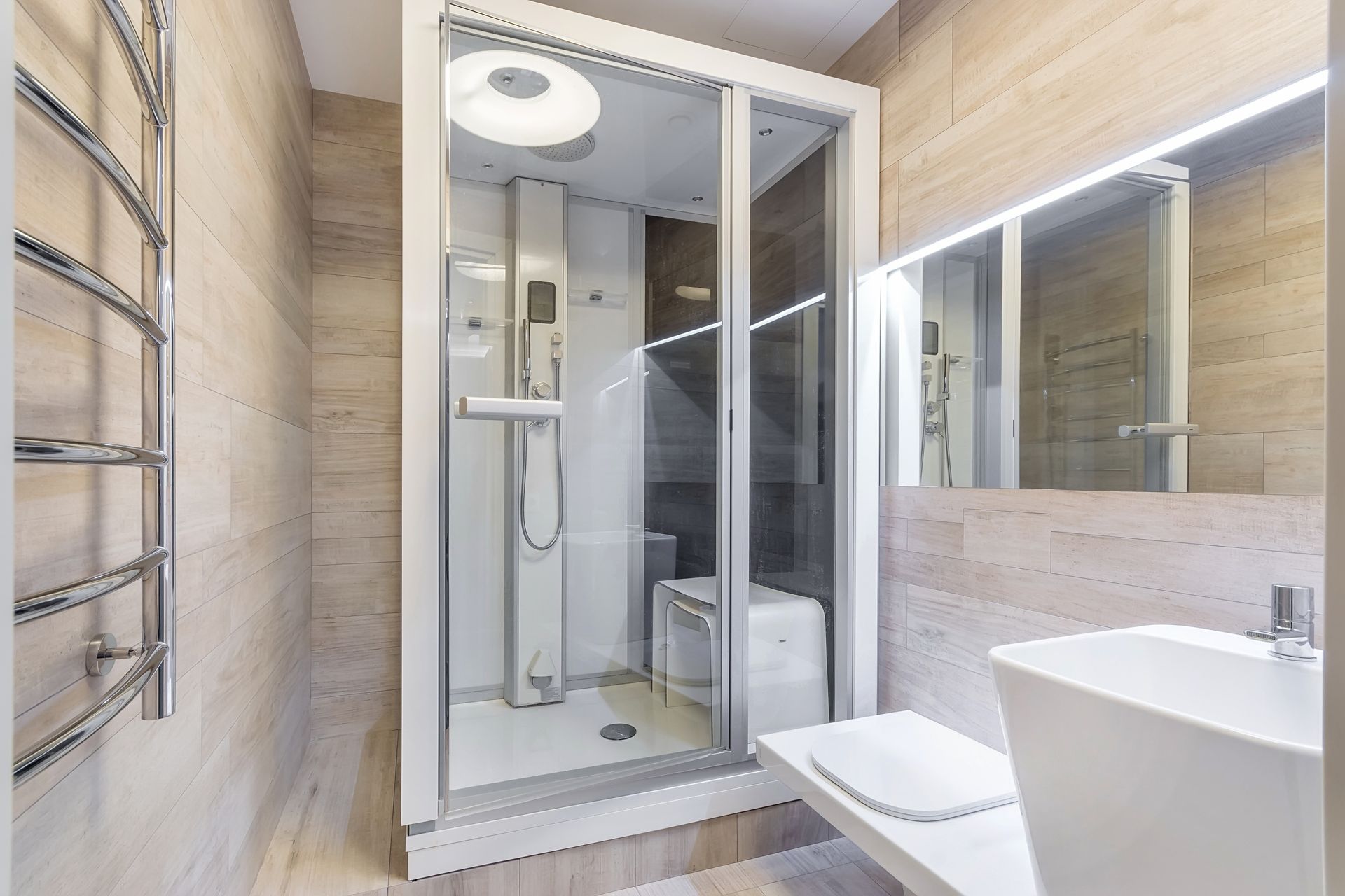 Modern bathroom with glass shower, wall mirror, sink, and toilet in beige tones
