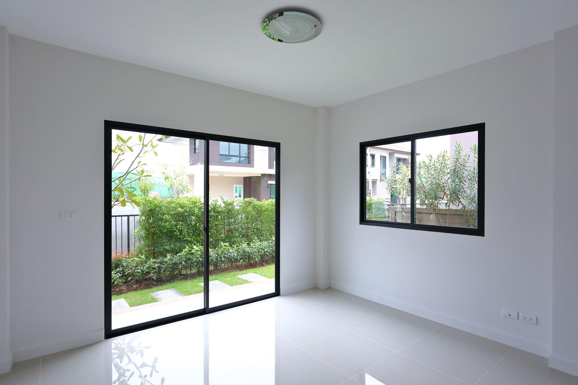 Empty modern room with white walls, glossy floor, and large windows overlooking greenery.