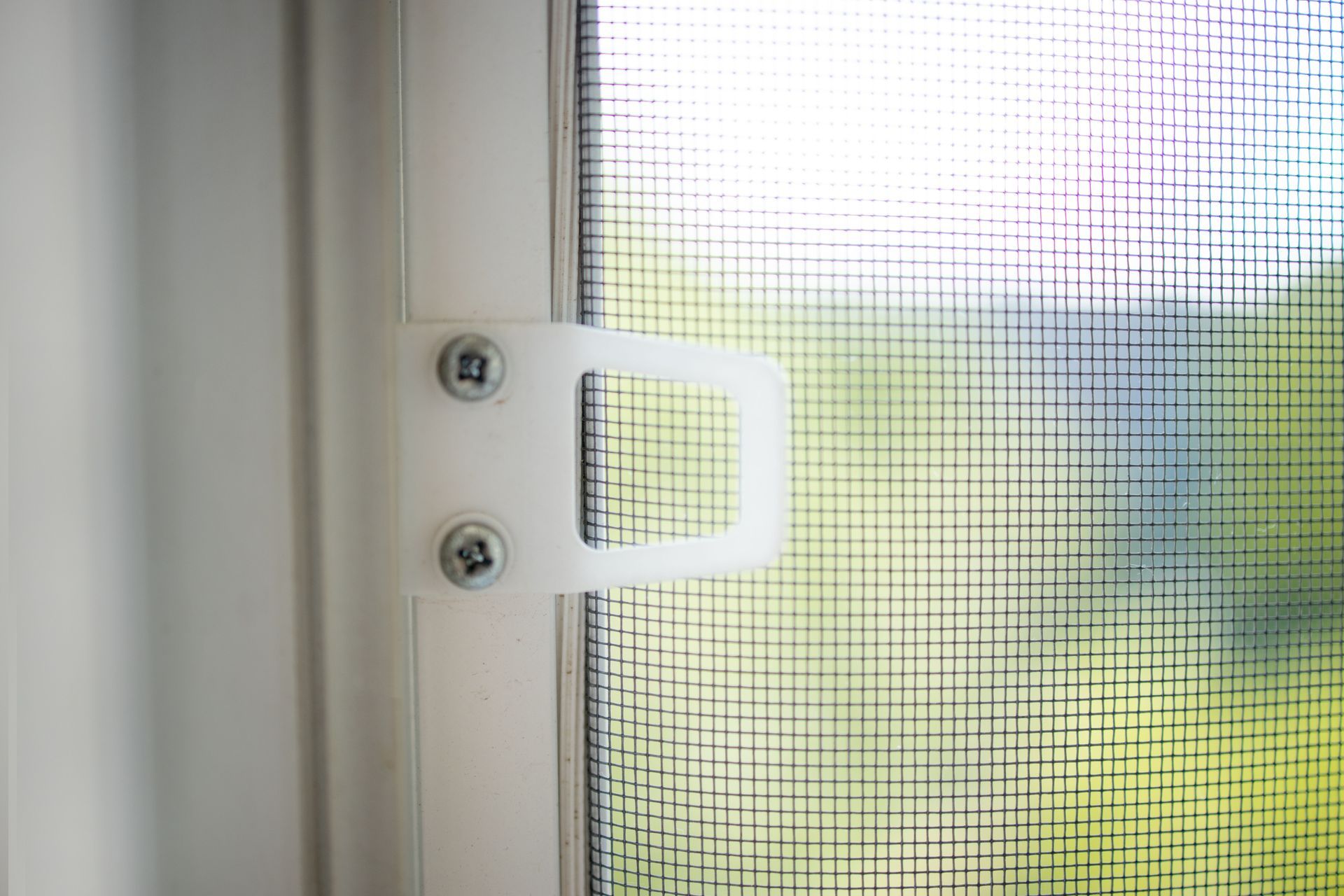 Close-up of a white window latch beside a screened window with bright outdoor light.