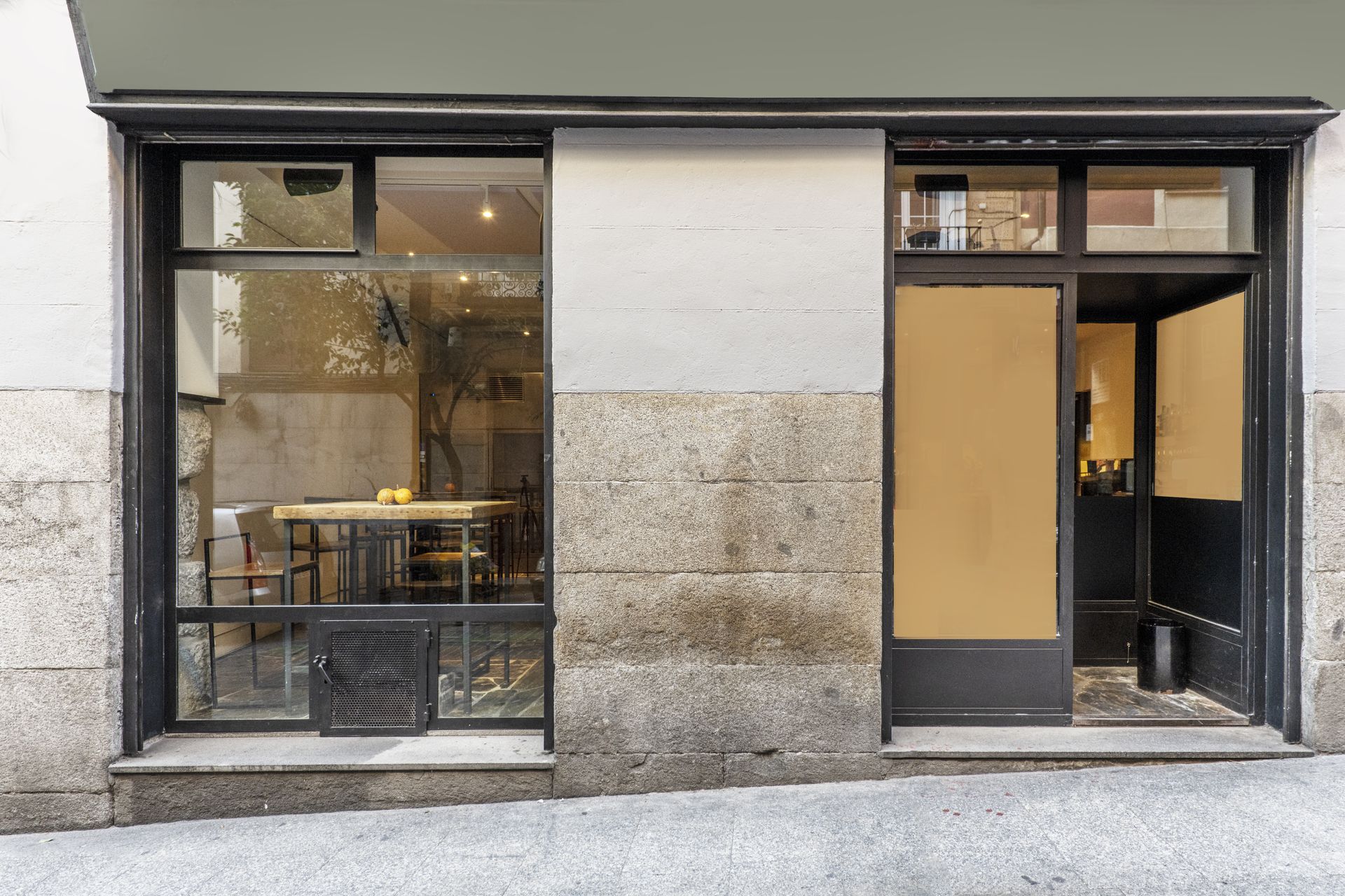 Modern storefront with large glass windows, gray stone facade, and a black-framed door.