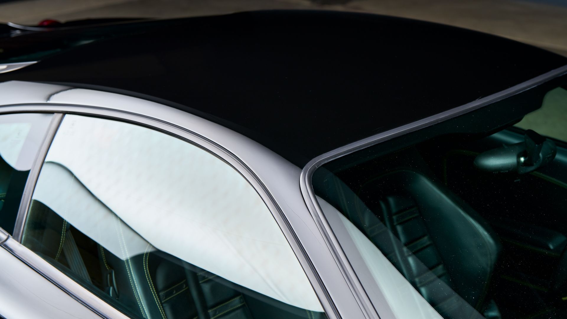 Close-up of a silver car’s side window and roofline with tinted glass and reflections