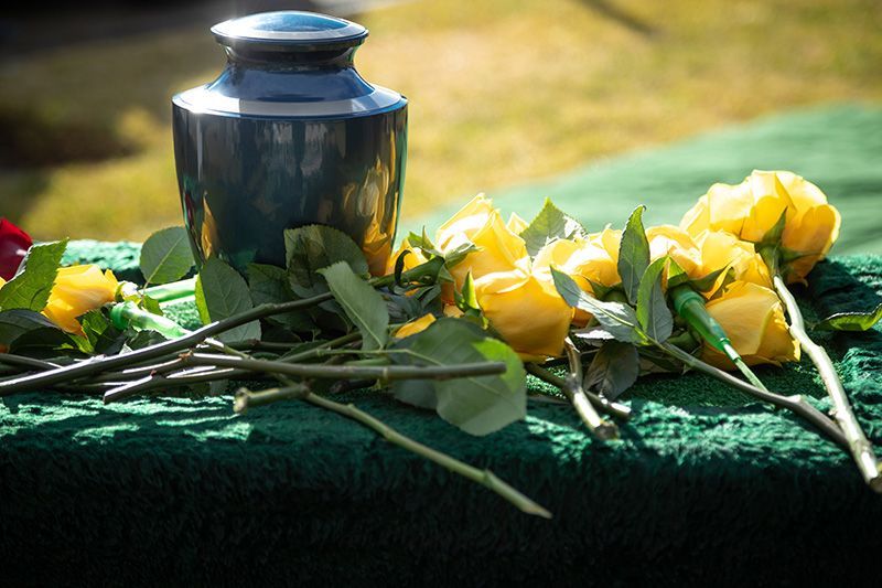 A dark blue urn next to yellow roses on a green surface at a memorial service.