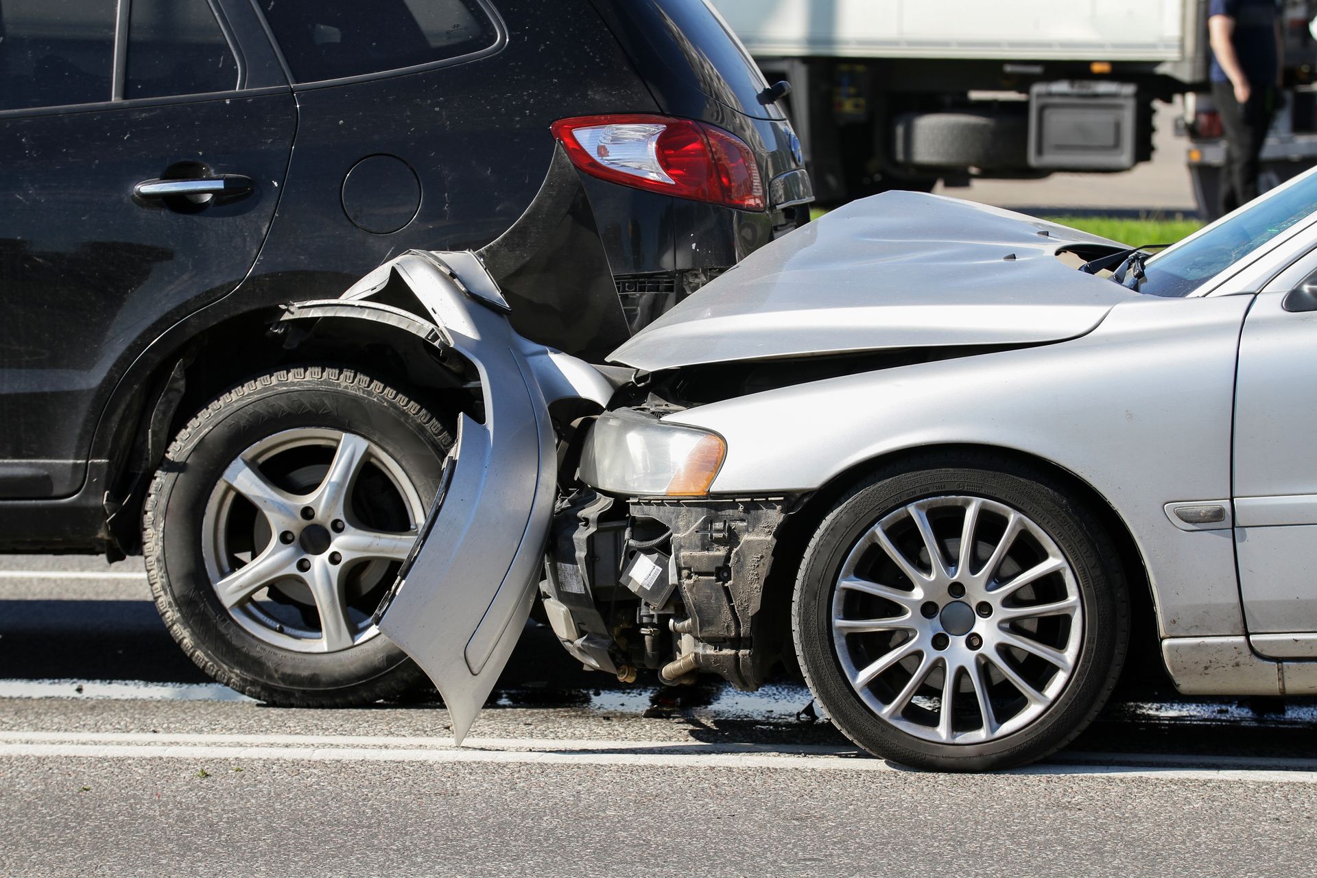 Two cars with heavy front-end collision damage on a road, one black and one silver. Two cars with heavy front-end collision damage on a road, one black and one silver.