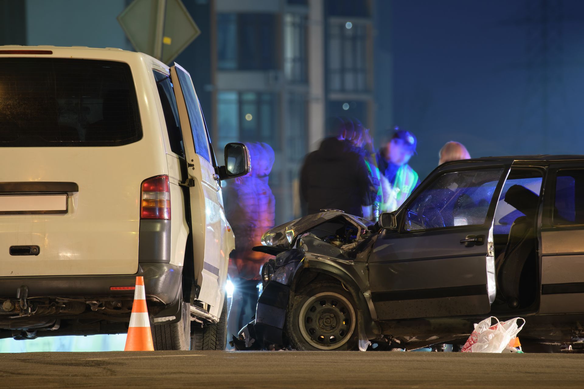 Severe nighttime car crash with a white van, damaged sedan, cones, and responders at the scene Severe nighttime car crash with a white van, damaged sedan, cones, and responders at the scene