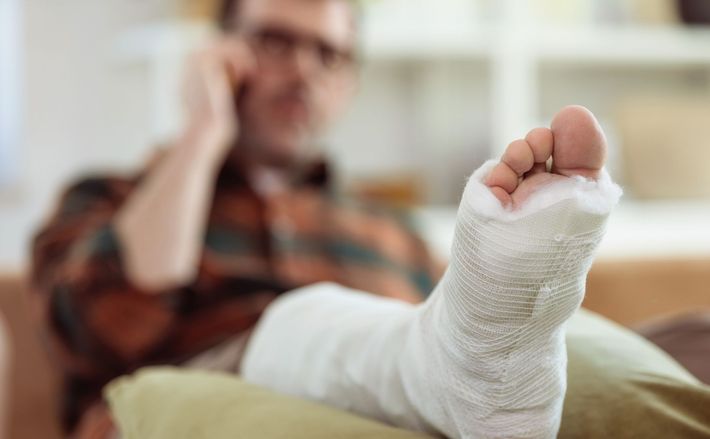 A man with a broken leg is sitting on a couch talking on a cell phone — Willmar, MN — Schneider & Madsen PC A man with a broken leg is sitting on a couch talking on a cell phone — Willmar, MN — Schneider & Madsen PC