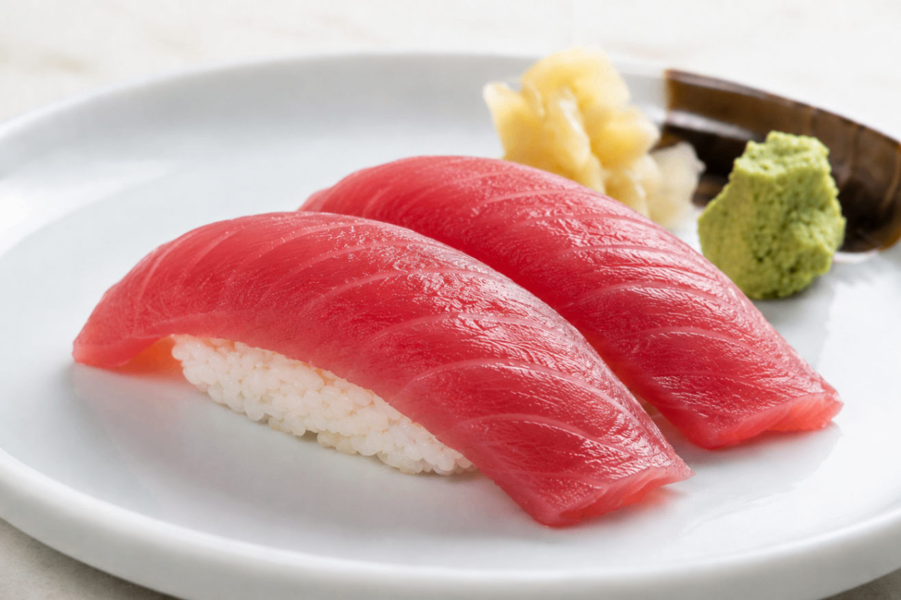 Two pieces of red tuna nigiri on a white plate with wasabi and ginger