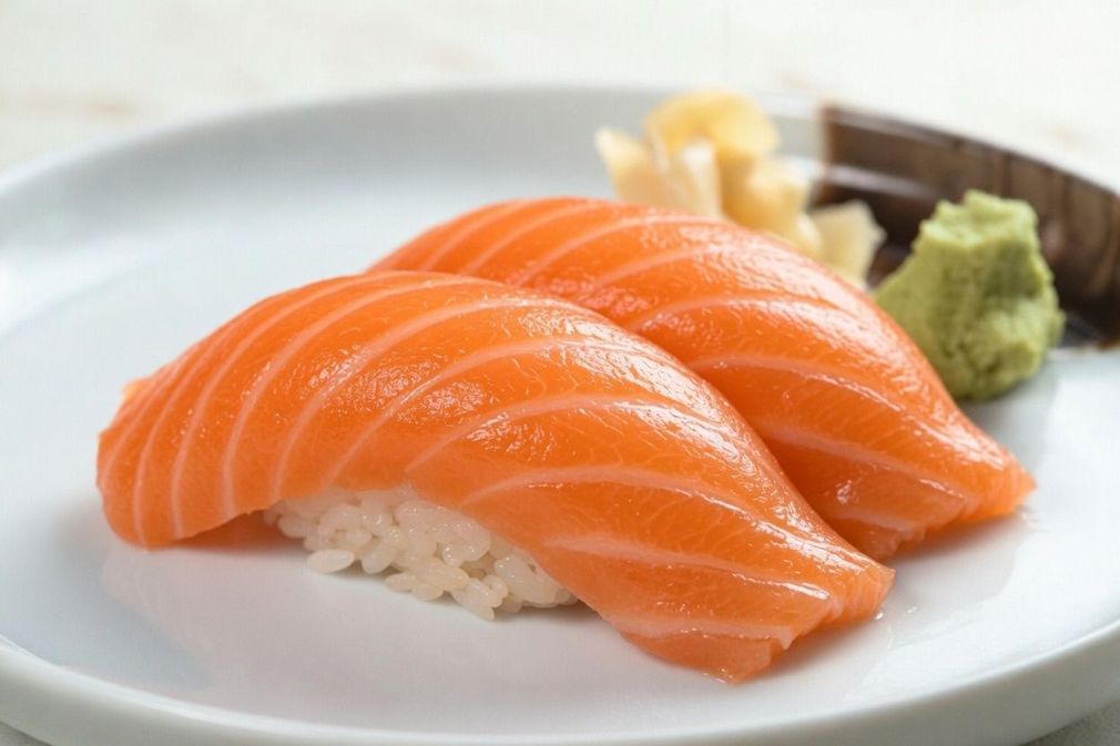 Salmon nigiri sushi on a white plate with wasabi and pickled ginger