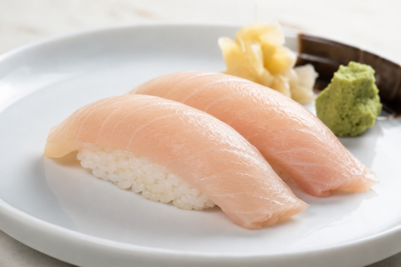 Two salmon nigiri sushi pieces on a white plate with wasabi and ginger garnish