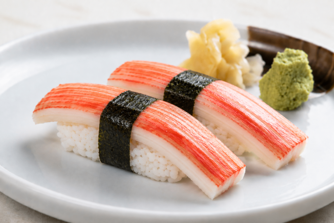 Crab stick sushi nigiri on a white plate with wasabi and pickled ginger