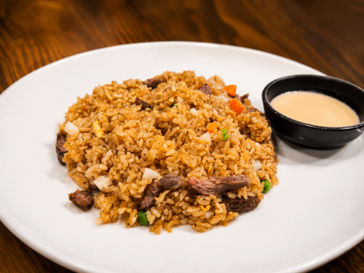 Plate of fried rice with vegetables and meat, served with a small bowl of creamy sauce