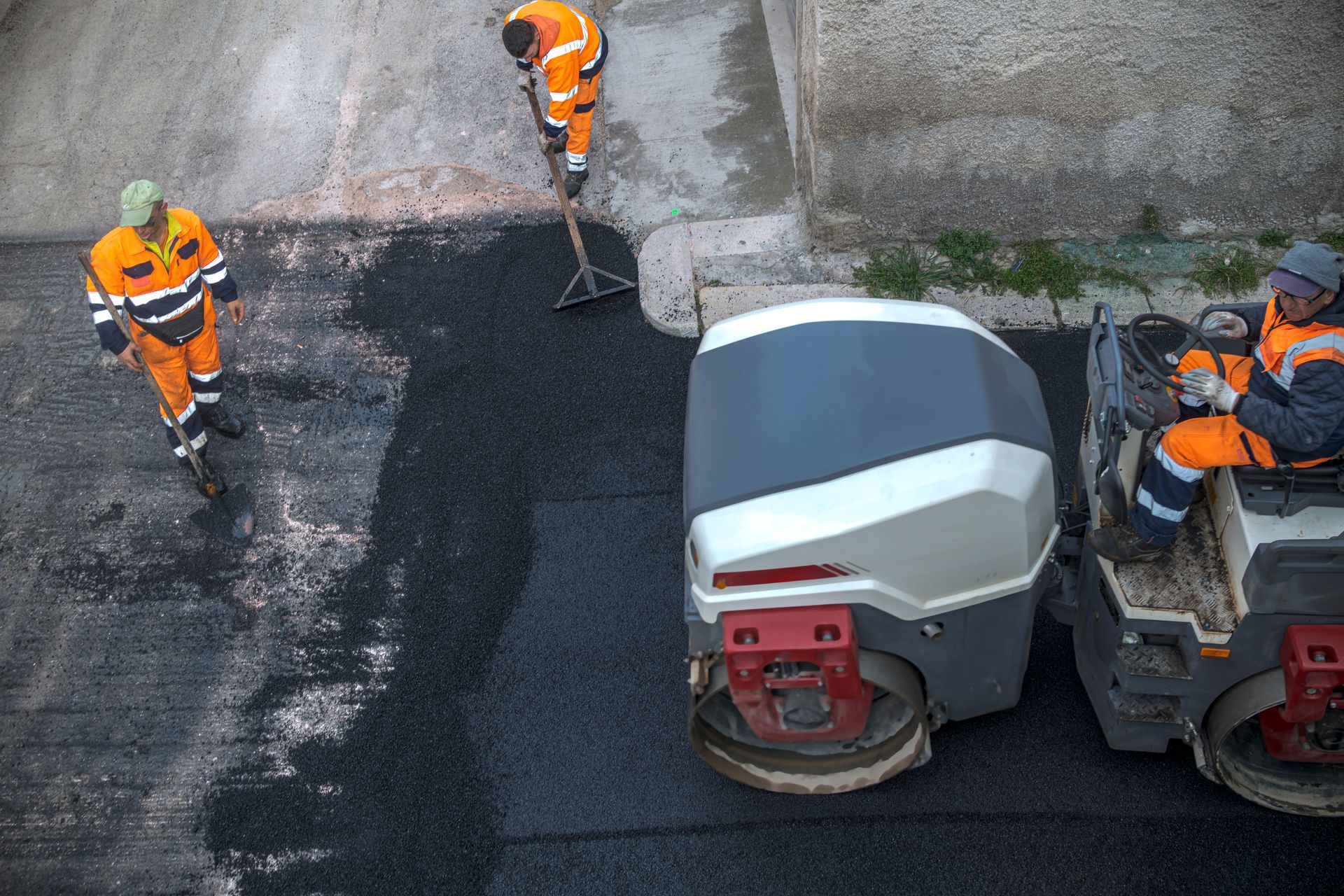 Photograph showing road construction workers paving asphalt on a street using a roller compactor and