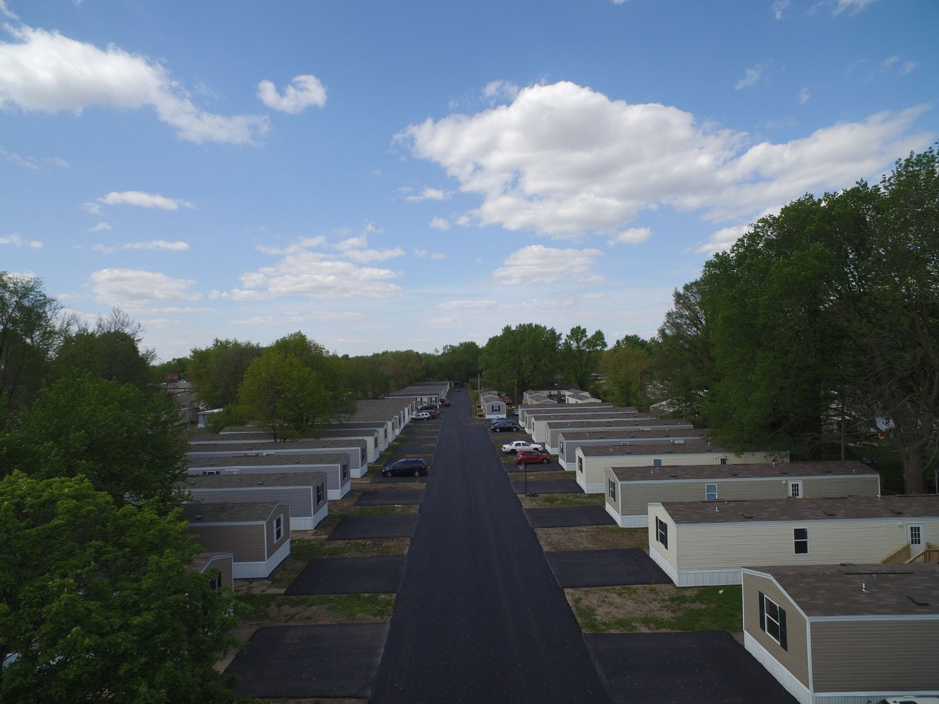 Aerial view of a mobile home park on a sunny day. Black asphalt road with parked cars and identical homes.