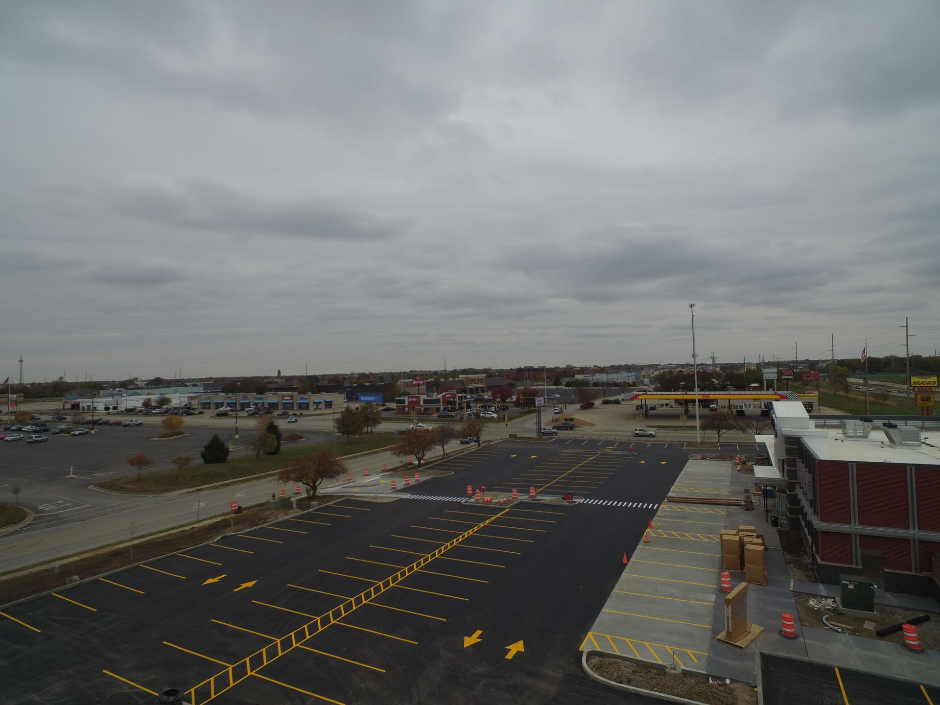 Overhead view of a large, empty parking lot with yellow parking space markings and a cloudy sky.