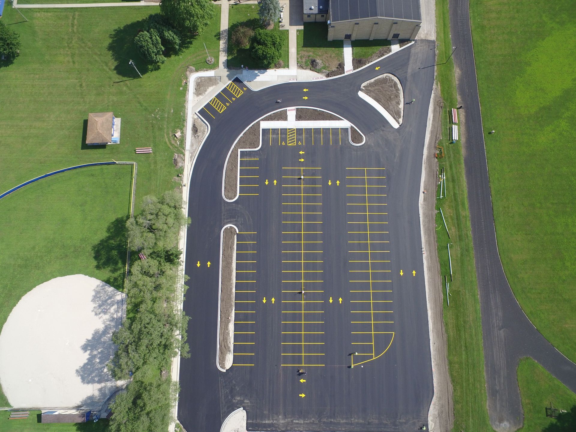 Aerial view of a newly paved parking lot with yellow parking lines, next to a grassy field.