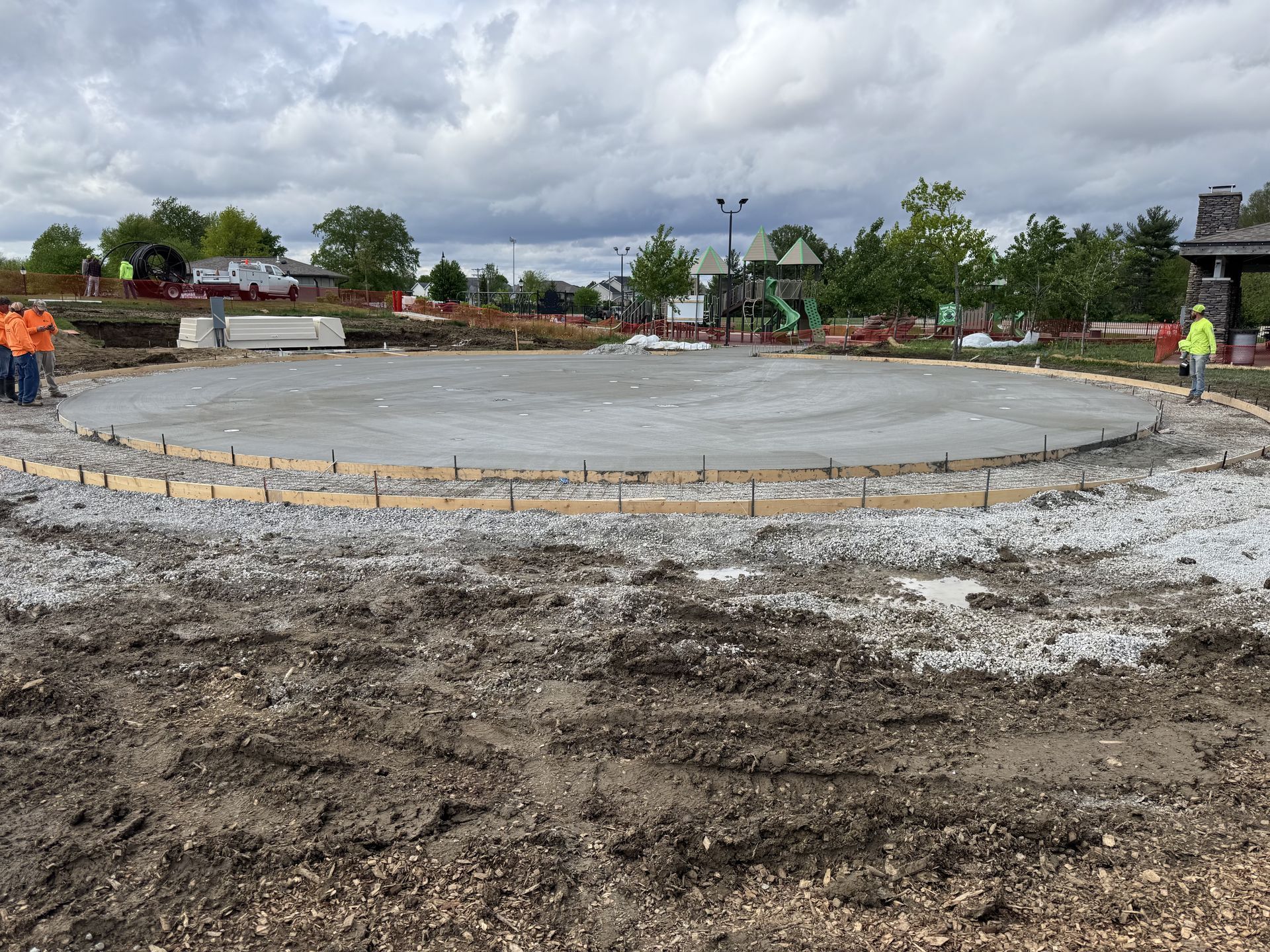 Construction site with a circular concrete slab, workers nearby under a cloudy sky.