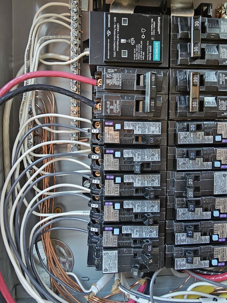 Open electrical breaker panel with rows of black breakers and bundled white and red wires.