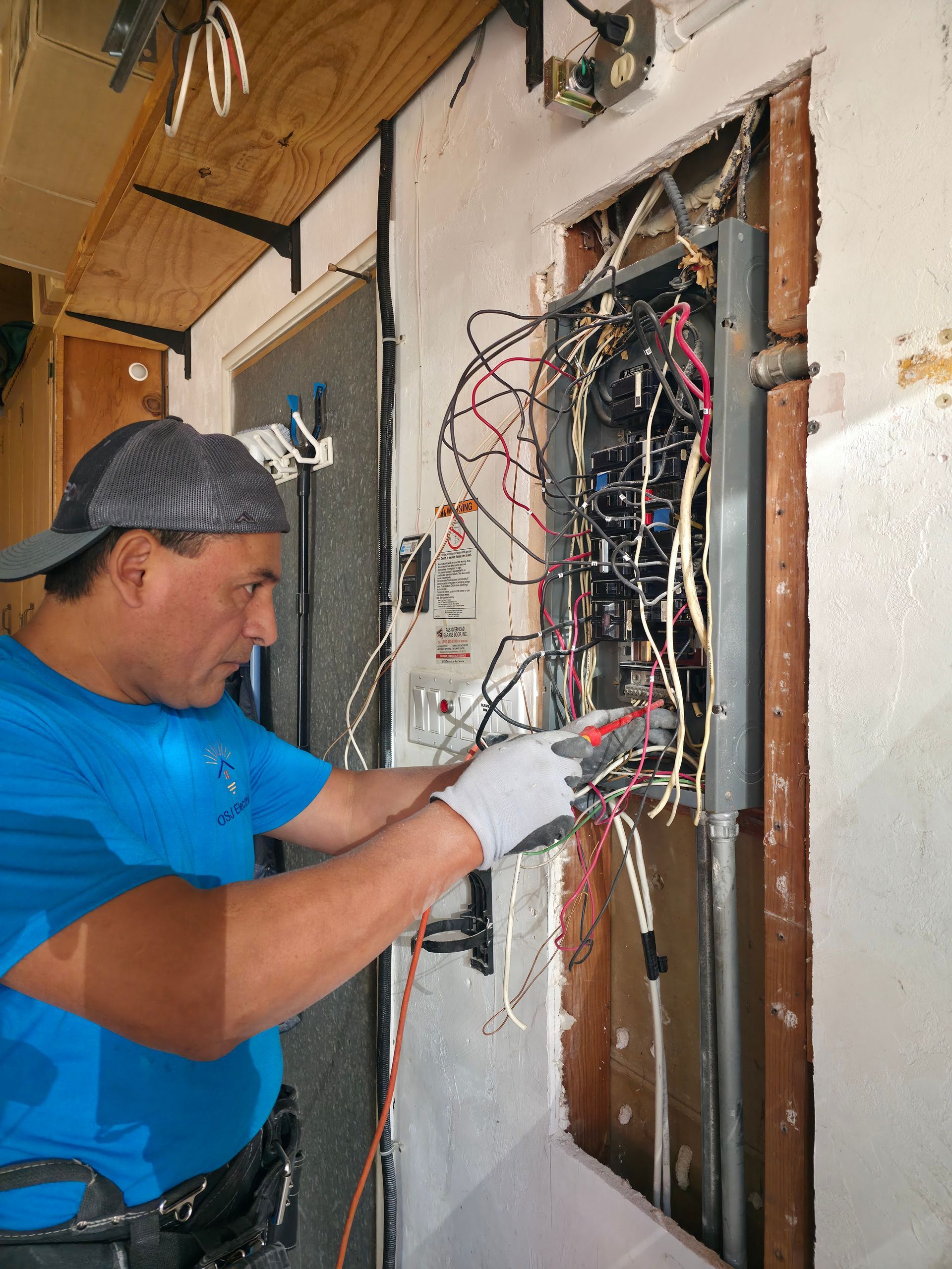 Electrician working on exposed wiring inside a wall panel indoors
