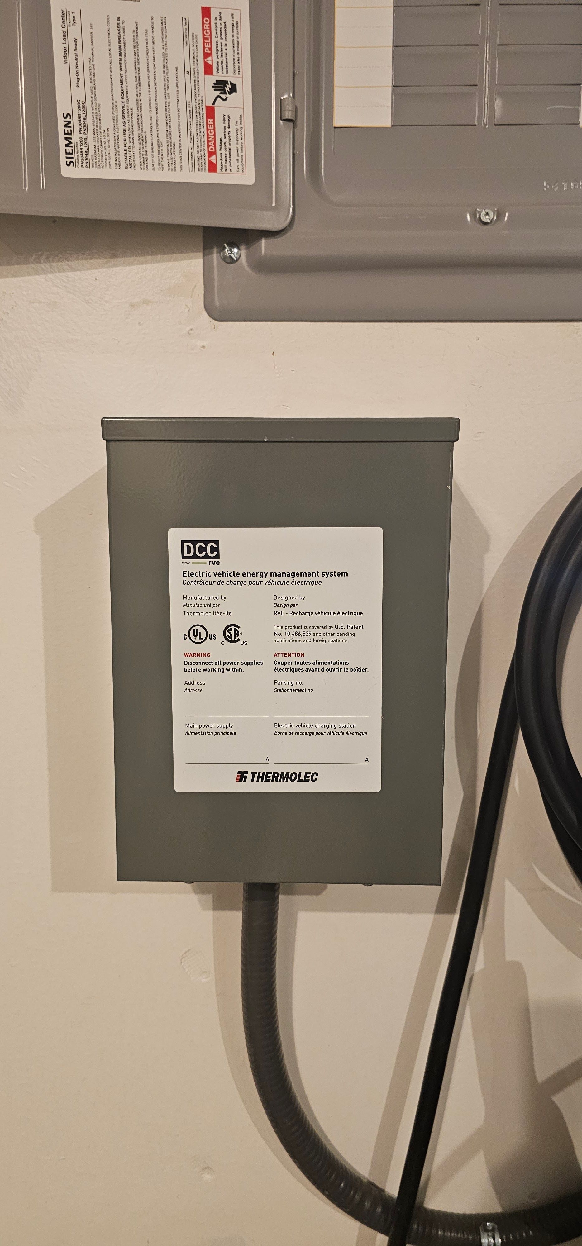 Gray electrical box with a white label and thick black cables mounted on a wall.