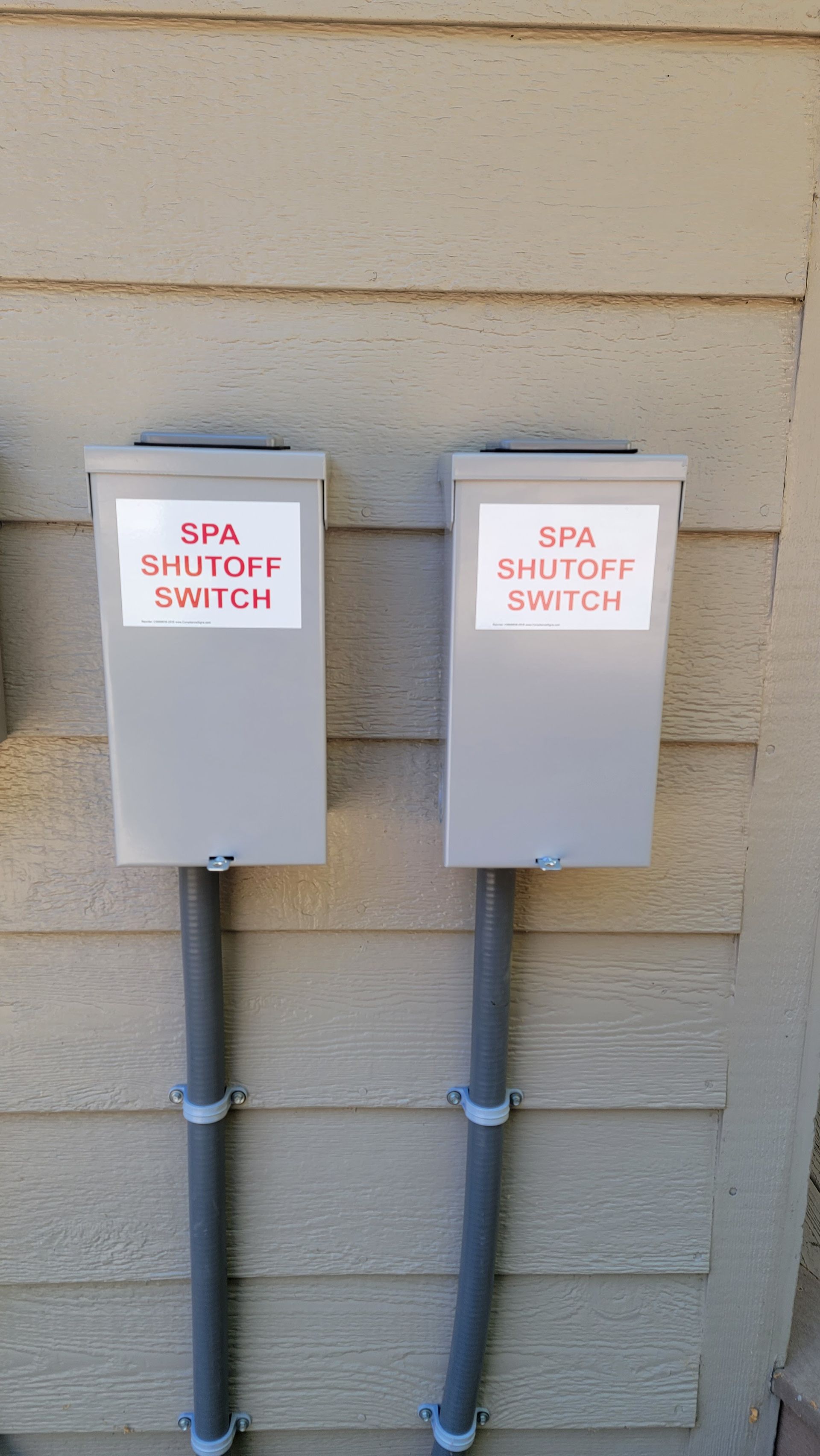 Two gray electrical shutoff switches mounted on beige siding with red labels.