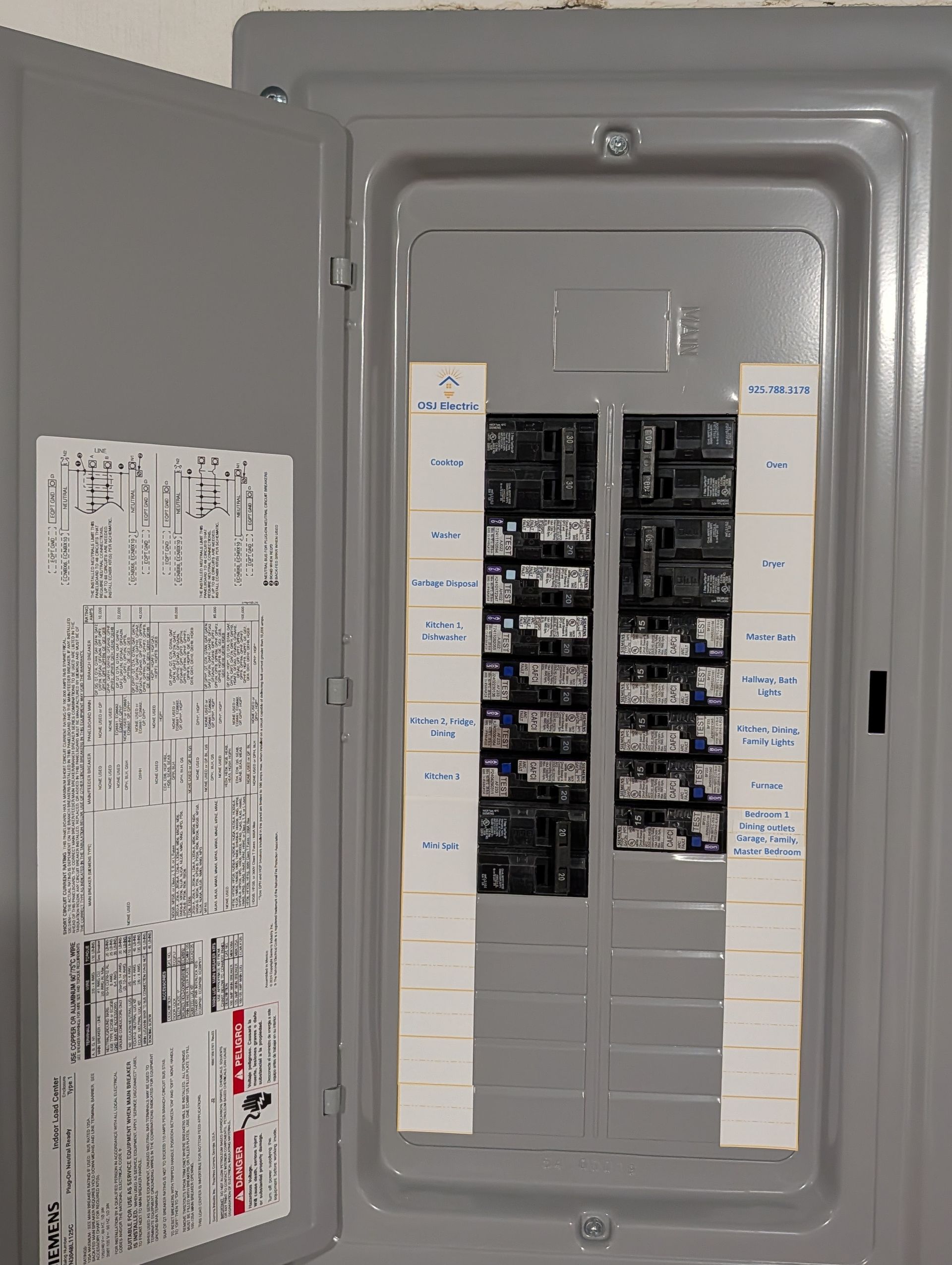 Open electrical breaker panel with multiple labeled circuit switches in a gray metal cabinet