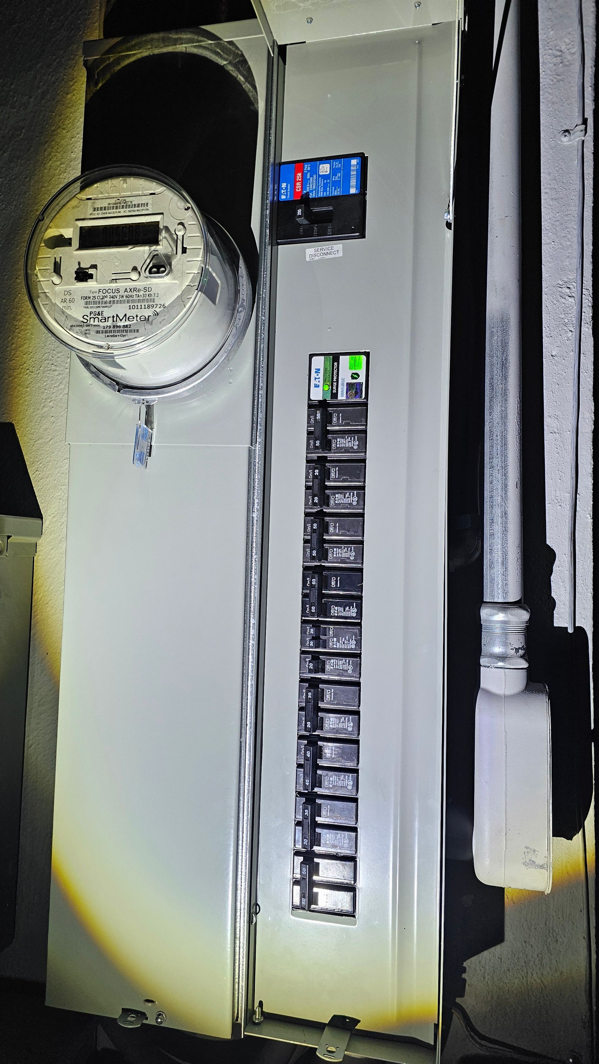 Electrical breaker panel with meter and switches on a wall, showing visible conduit and wiring.